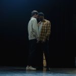 Dois atores ensaiam uma cena intensa em um palco pouco iluminado.