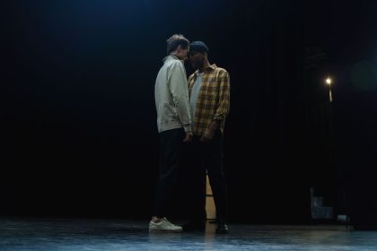 Dois atores ensaiam uma cena intensa em um palco pouco iluminado.
