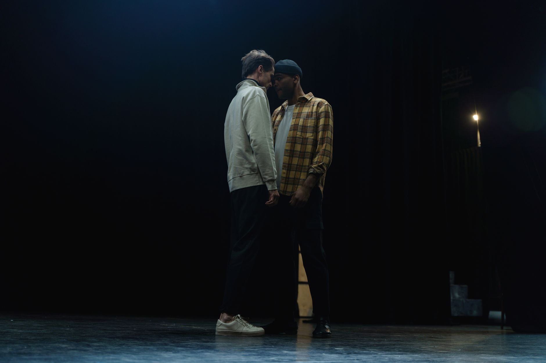 Dois atores ensaiam uma cena intensa em um palco pouco iluminado.