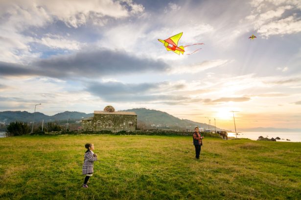 Uma criança e um adulto empinam pipas em uma paisagem rural ao pôr do sol.