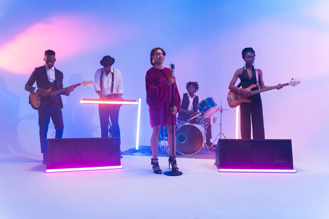 Banda se apresenta em um palco iluminado por luzes coloridas, com instrumentos musicais ao fundo.