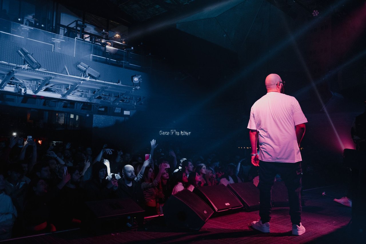 Rapper se apresenta em um palco iluminado diante de uma plateia durante um show.