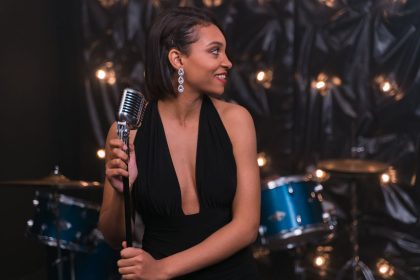 Cantora se apresenta ao microfone em um palco, com uma bateria ao fundo.