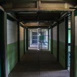 Corredor de uma prisão vazio, com portas de celas abertas e iluminação sombria.