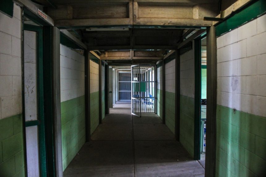 Corredor de uma prisão vazio, com portas de celas abertas e iluminação sombria.