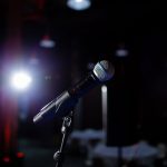 Microfone em um palco iluminado por um refletor, preparado para uma apresentação ao vivo.
