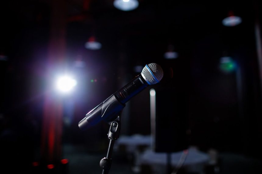 Microfone em um palco iluminado por um refletor, preparado para uma apresentação ao vivo.