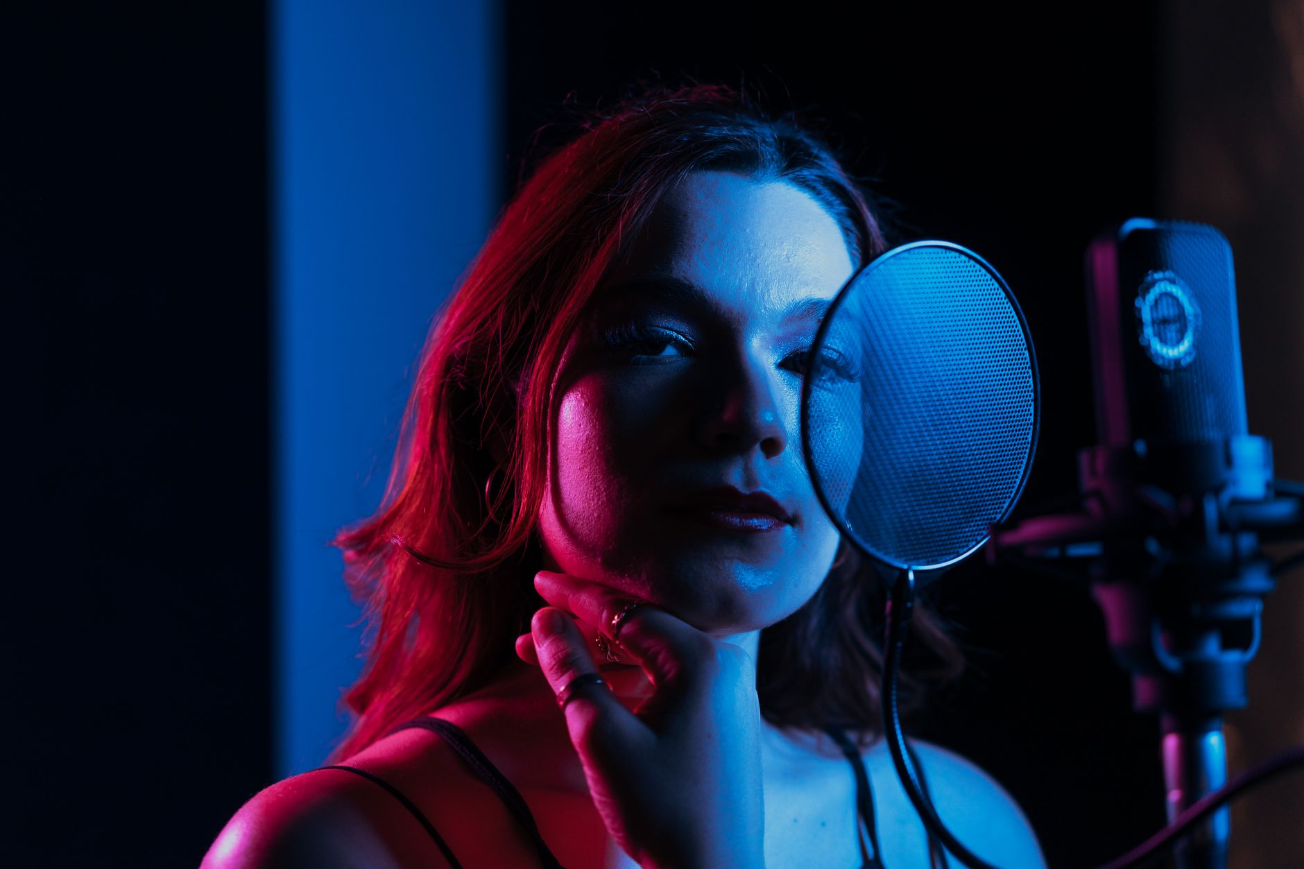Cantora grava vocais diante de um microfone em um estúdio iluminado com luzes coloridas.